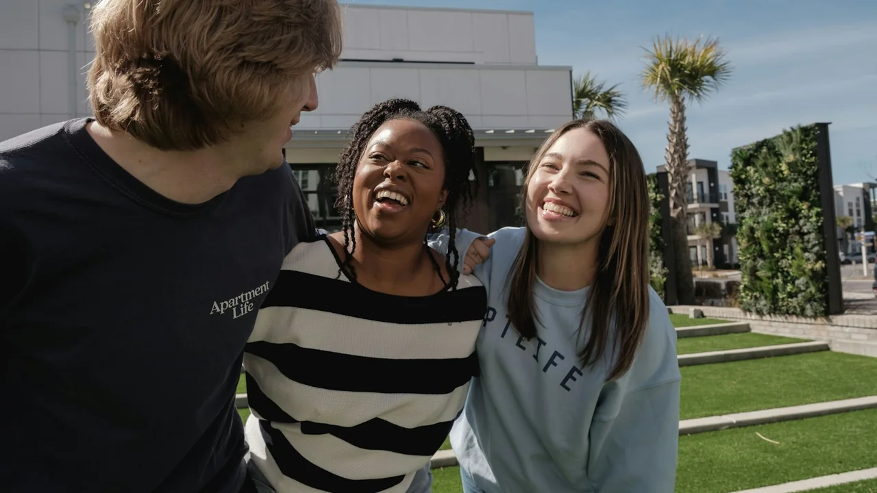 Drei junge Leute lachen gemeinsam draußen in der Sonne – Symbolbild für mehr echte Zeit statt Bildschirmzeit