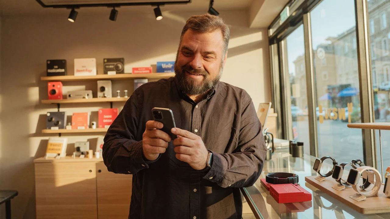 Christian Rill im greem-Shop hält eine Smartwatch hoch, davor eine kleine Auslage mit Wearables
