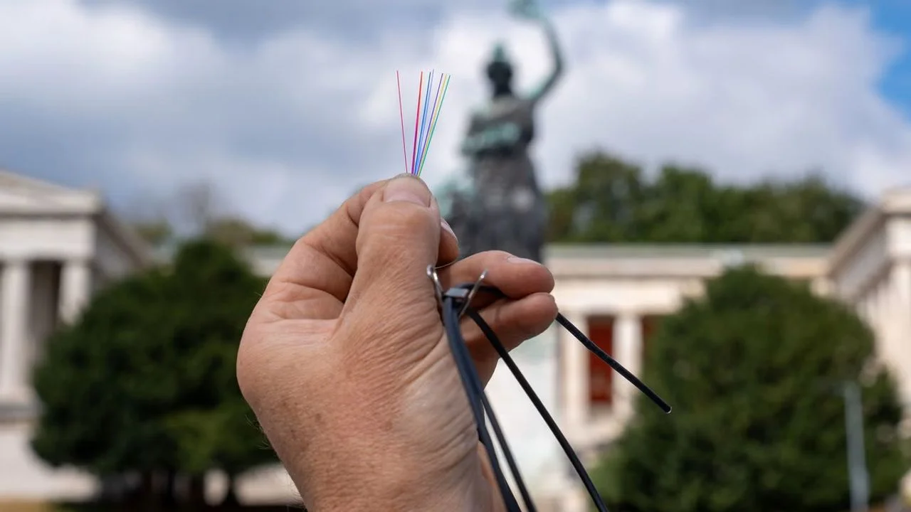 Hand hält Glasfaserkabel vor der Bavaria-Statue auf der Münchner Theresienwiese