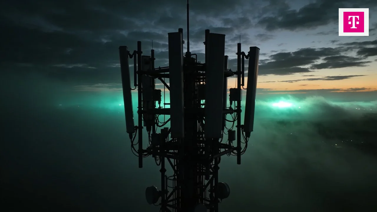 Mobilfunkmast mit Antennen in der D&auml;mmerung &uuml;ber Nebel, oben rechts das Telekom-Logo